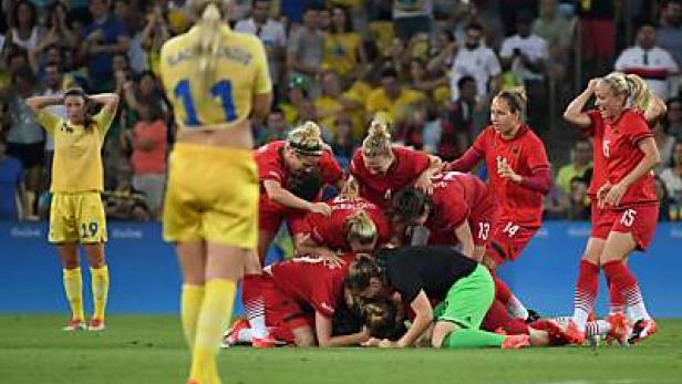 Fußballspielerinnen in roten Trikots feiern einen Sieg, während eine Spielerin in Gelb traurig daneben steht.
