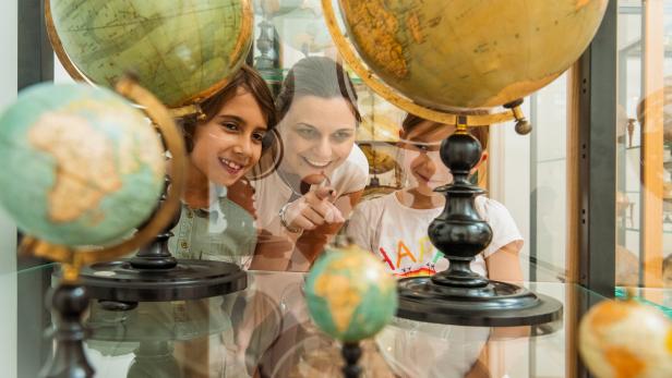 Eine Frau zeigt auf einen Globus, während zwei Mädchen lächeln.