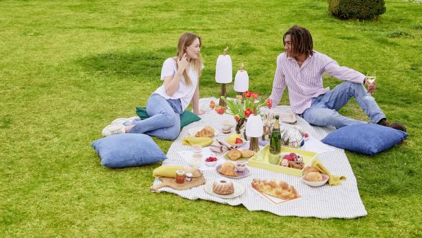 Ein Paar genießt ein Picknick mit Gebäck und Getränken auf einer Wiese.