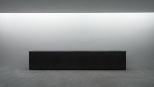 Ein langer, schwarzer Schrank steht vor einer hellen Wand.