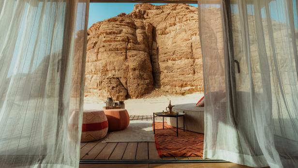 Blick aus einem Zelt auf eine Sandlandschaft mit einem markanten Felsen.