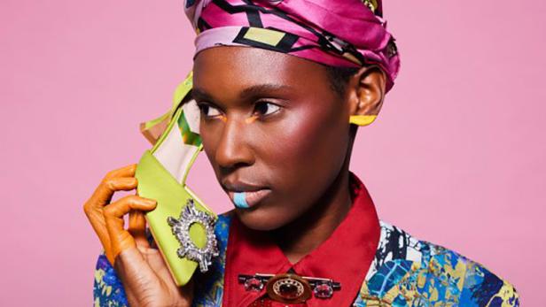 Eine Frau mit einem bunten Turban hält einen grünen Schuh am Ohr.