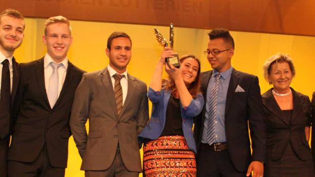 Eine Gruppe von Personen posiert mit einer goldenen Trophäe auf einer Bühne.