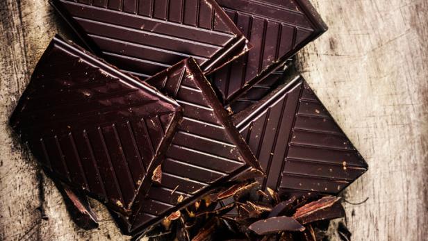 Mehrere Stücke dunkler Schokolade liegen auf einem Holztisch.