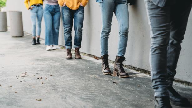 Eine Gruppe von Menschen steht an einer Wand aneinandergereiht.