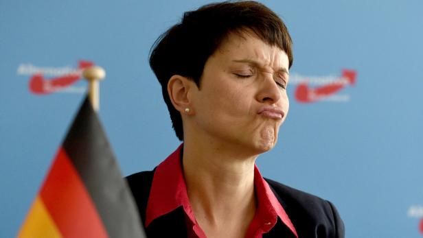 Eine Frau mit zusammengekniffenen Augen und Schmollmund steht vor einem AfD-Logo und einer Deutschlandflagge.