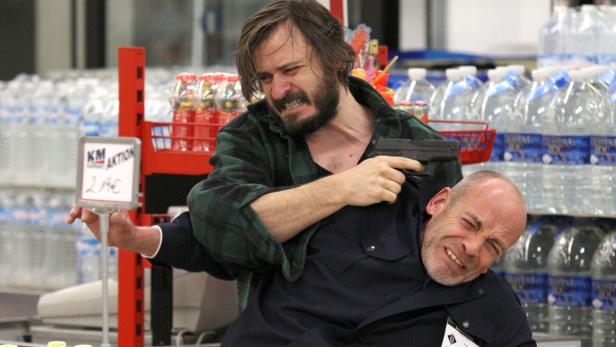Ein Mann bedroht einen anderen Mann mit einer Pistole in einem Supermarkt.