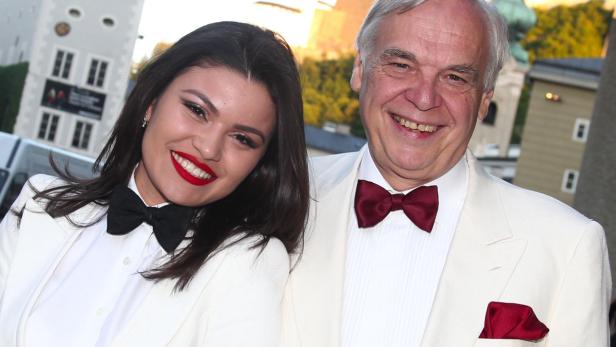 Eine lächelnde Frau mit rotem Lippenstift und ein Mann mit Fliege posieren für ein Foto.