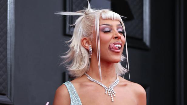 Doja Cat in einem hellblauen, glitzernden Kleid auf dem roten Teppich, die Zunge herausstreckend.