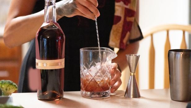 Eine Frau mit Tätowierung rührt einen Cocktail in einem Glas mit Eis.