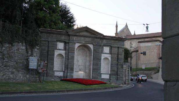 Ein steinernes Bauwerk mit roten Blumen an einer Straßenecke.
