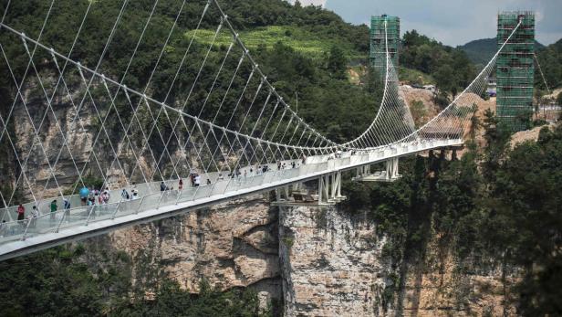 Eine Hängebrücke überspannt eine tiefe Schlucht, auf der Menschen zu sehen sind.