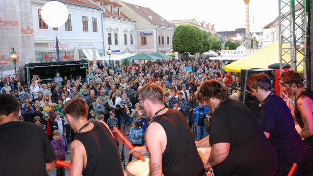Eine Trommlergruppe tritt vor einer großen Menschenmenge auf einem Stadtplatz auf.