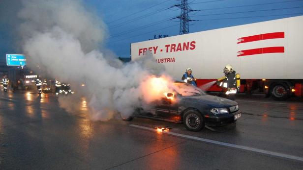 Ein brennendes Auto wird von Feuerwehrleuten auf einer Autobahn gelöscht.