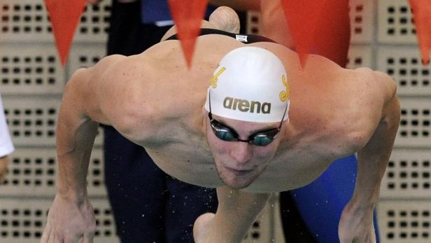 Ein Schwimmer mit Badekappe und Schwimmbrille springt ins Wasser.
