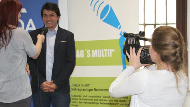 Ein Mann wird vor einem Banner mit der Aufschrift „Sag’s multi!“ interviewt.