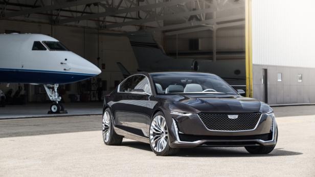 Ein dunkler Cadillac steht vor einem Hangar mit Privatjets.