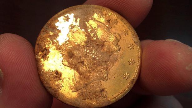 Eine goldene Liberty Head Münze aus dem Jahr 1890, die von Fingern gehalten wird.