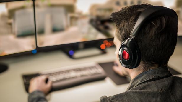 Ein Mann mit Kopfhörern spielt ein Computerspiel auf zwei Monitoren.