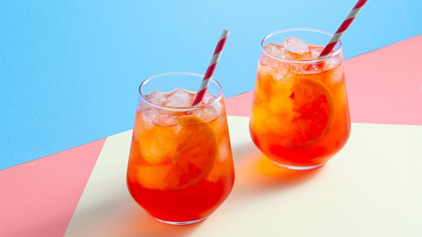 Spritz-Cocktails in Gläsern mit Eis und Orangenscheibe auf trendigem, farbenfrohem Hintergrund. Kreatives, minimales Konzept.
