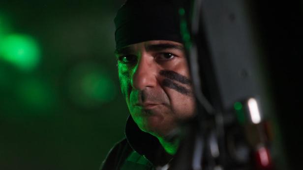 Ein Mann mit Kriegsbemalung und schwarzer Mütze blickt ernst in die Kamera.