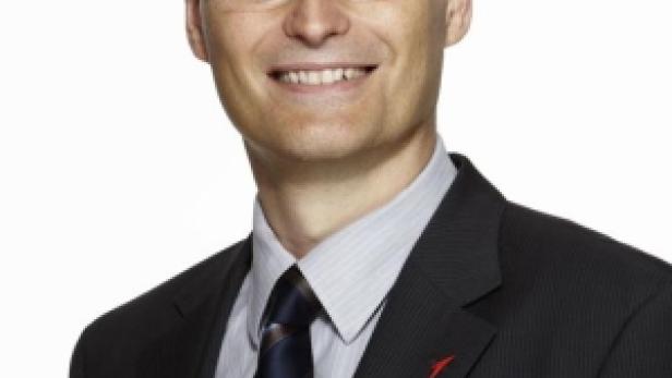 Ein Mann mit Brille und Anzug lächelt in die Kamera.