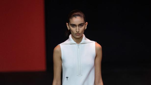 Eine Frau in einem weißen Dior-Kleid mit Faltenrock und passenden Stiefeln auf dem Laufsteg.