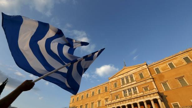 Eine Person hält eine griechische Flagge vor dem griechischen Parlament.