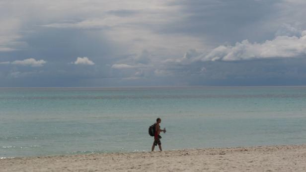 Ein Mann mit Rucksack geht am Strand entlang.