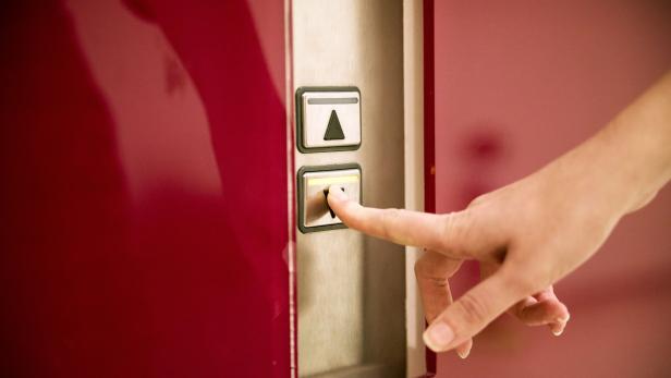 Eine Frau drückt den Abwärtsknopf in einem Aufzug.