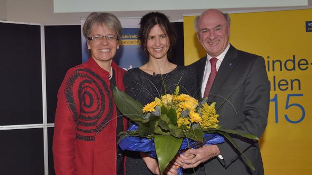Drei Personen posieren mit einem Blumenstrauß vor einem gelben Hintergrund.