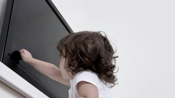 Ein kleines Kind berührt einen Flachbildfernseher.