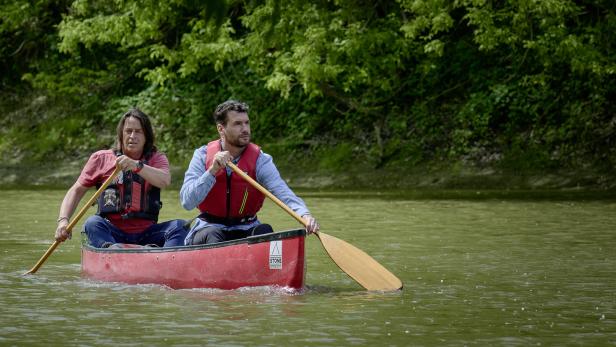 Zwei Männer paddeln in einem roten Kanu auf einem Fluss.