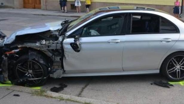 Ein silbernes Auto mit schweren Schäden an der Vorderseite steht am Straßenrand.