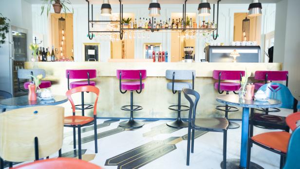 Innenansicht einer Bar mit Hockern und Tischen.