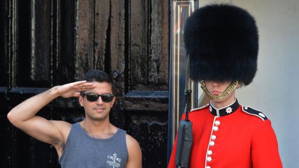 Ein Mann in Sonnenbrille salutiert neben einem Gardesoldaten in London.