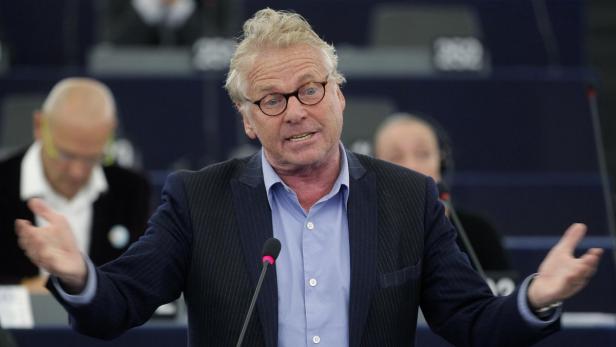 Ein Mann mit Brille gestikuliert während einer Rede vor einem Publikum.