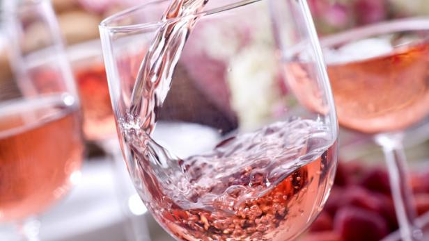 Roséwein wird in ein Glas gegossen, Erdbeeren und Blumen im Hintergrund.
