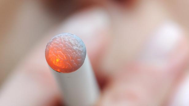 Nahaufnahme einer E-Zigarette, deren Spitze orange leuchtet.