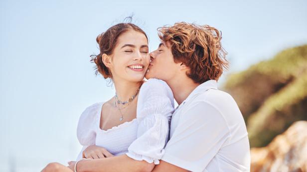 Ein junges Paar umarmt sich; der Mann küsst die Frau auf die Wange.