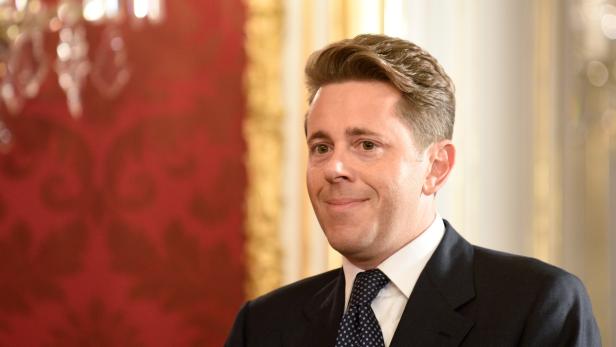 Ein Mann im Anzug lächelt vor einem roten Hintergrund.