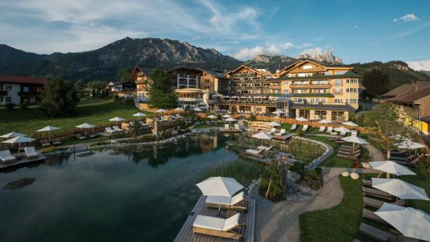 Ein luxuriöses Hotelresort mit einem See und Liegestühlen vor einer Bergkulisse.
