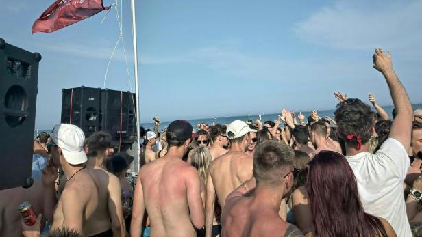 Eine Menschenmenge feiert am Strand unter einer österreichischen Flagge.