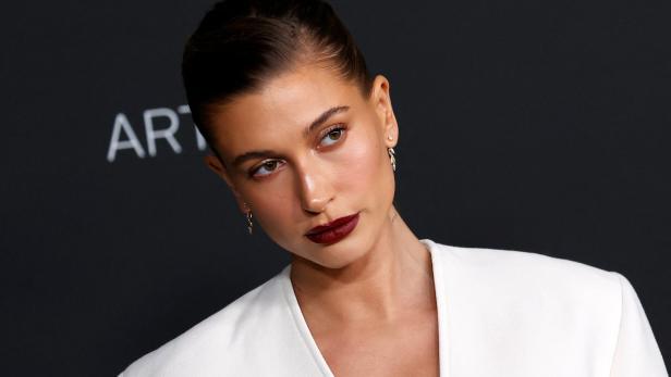 Hailey Bieber bei einer Veranstaltung mit dunklem Lippenstift und weißem Blazer.