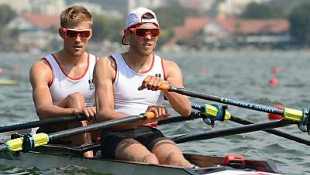Zwei Ruderer mit Sonnenbrillen in einem Rennboot auf dem Wasser.