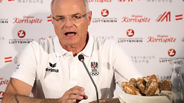 Ein Mann mit Brille spricht bei einer Pressekonferenz, im Hintergrund Werbung für Kornspitz.