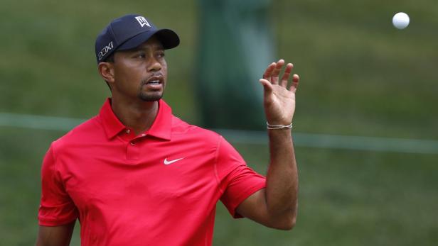 Tiger Woods in rotem Hemd wirft einen Golfball in die Luft.