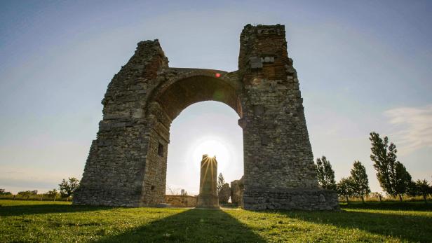 Die Ruine eines römischen Triumphbogens mit einem Obelisken im Gegenlicht.
