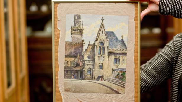Eine gerahmte Aquarellmalerei eines historischen Gebäudes mit Turm wird gehalten.
