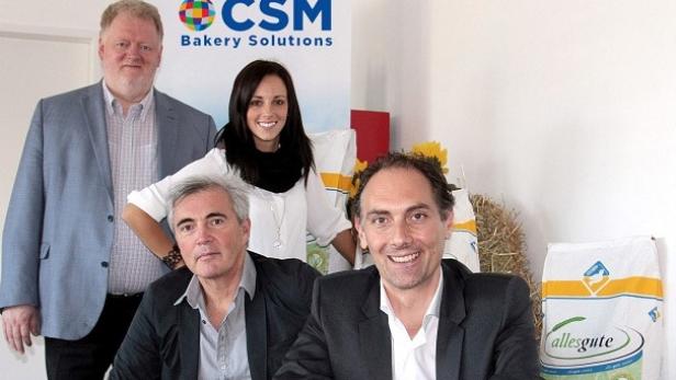 Eine Gruppe von vier Personen posiert vor einem Banner von CSM Bakery Solutions.